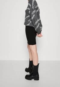 Grå tröja med vit text, svart ribbat minikjol och svarta klumpiga ankelstövlar med klack. Modell stående sidledes mot en ljus bakgrund.