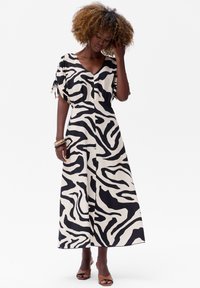 Zwart-witte maxi-jurk met zebrapatroon, korte mouwen, V-hals en gathered details bij de schouders, gemaakt van een lichte stof.