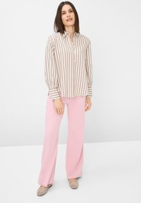 Camicia abbottonata a maniche lunghe a righe verticali beige e bianche, abbinata a pantaloni rosa chiaro a gamba larga e scarpe flat color taupe.