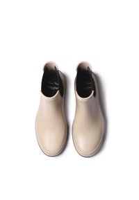 Botas de tobillo de goma beige con un acabado liso, punta redondeada, paneles laterales elásticos y un forro interior texturizado. Logotipo negro visible en el interior.