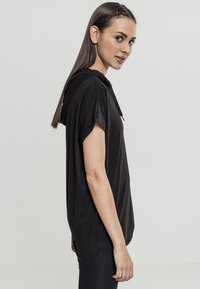 Svart huva t-shirt gjord av mjuk tyg, med korta ärmar, en avslappnad passform och en asymmetrisk kant.