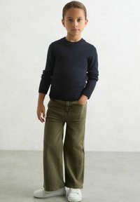 Maglione blu navy a maglia con polsini a costine abbinato a pantaloni larghi color verde oliva. Sneakers bianche completano l'outfit. Stile semplice e casual.