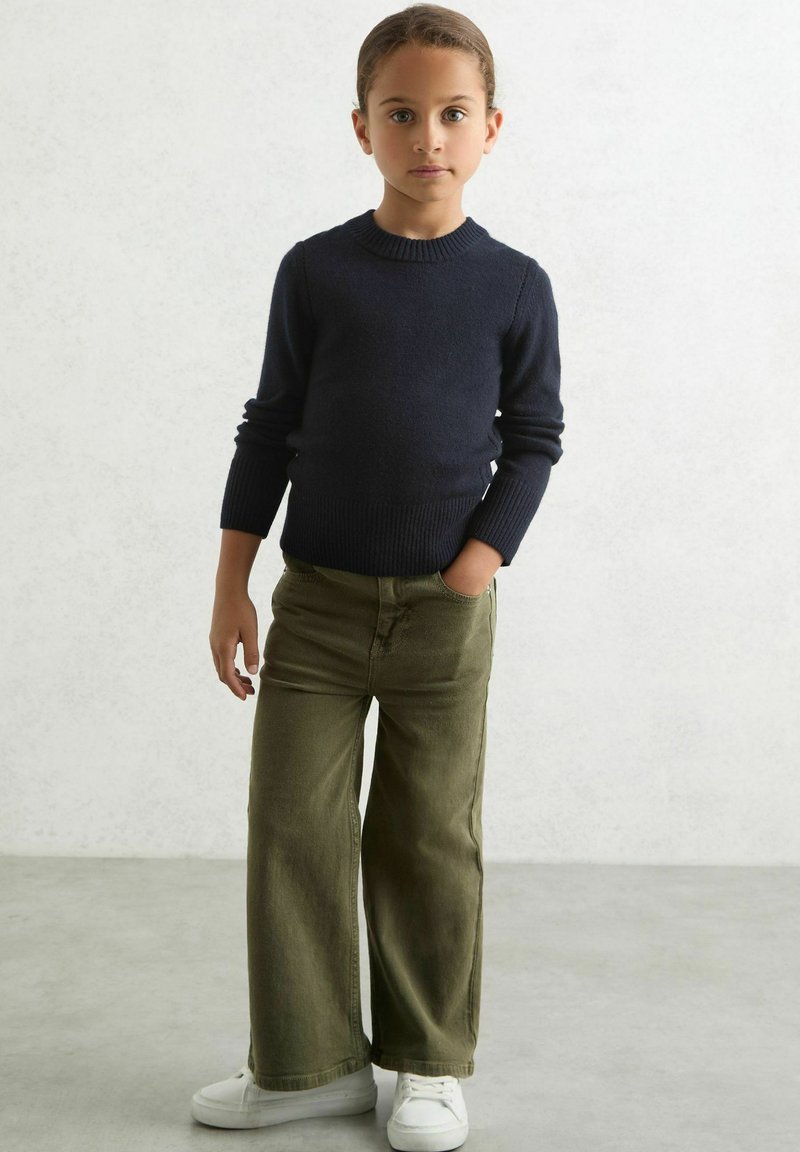 Maglione blu navy a maglia con polsini a costine abbinato a pantaloni larghi color verde oliva. Sneakers bianche completano l'outfit. Stile semplice e casual.