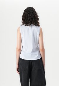 Ermeløs bluse i lyseblå stripet stoff med en tettsittende design. Kombinert med svarte løse shorts, som viser en avslappet stil.