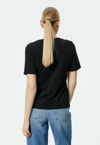 Sort bomulds T-shirt med korte ærmer, rund hals og lige snit. Bæres sammen med lyseblå denim jeans.