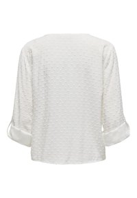 Blouse blanche avec un motif à pois texturé, manches trois-quarts avec des poignets retroussés, et une coupe décontractée. Tissu lisse avec un léger brillant.