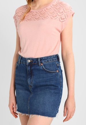 Donna che indossa un top a maniche corte rosa pallido con dettagli in pizzo e una gonna di jeans blu a vita alta con orlo strappato.