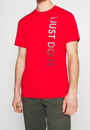 Homme portant un T-shirt rouge à manches courtes avec un texte vertical blanc et noir "JUST DO IT." et un petit logo Nike swoosh blanc sur la poitrine.