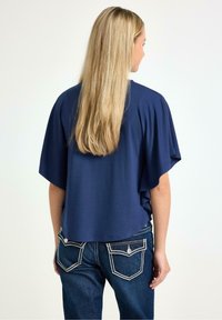 Marinblå kortärmad topp med avslappnad passform, kombinerad med mörkblå jeans med framträdande vita sömmar på bakfickorna.