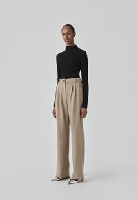 Sort ribbet turtleneck sweater parret med højtaljede beige plisserede bukser og sølvfarvede spidse hæle. Enkel og struktureret design.