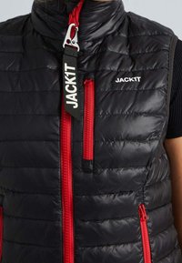 Schwarze gepolsterte Weste mit roten Reißverschlüssen und Branding. Hat einen hohen Kragen, horizontale Nähte und zwei seitliche Taschen mit Reißverschluss.