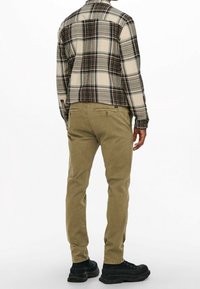 Ruteret flannel skjorte i beige og blå, båret over olivenfarvede chinos. Sorte støvler fuldender outfittet. Skjorten har en knap-ned krave.
