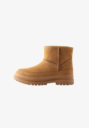 Botte mi-mollet en daim beige avec semelle épaisse en caoutchouc à crampons et coutures visibles, conçue pour un usage décontracté.