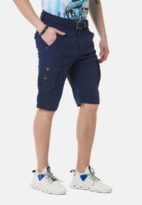 Marine cargo shorts met meerdere zakken en knopen, voorzien van een gevlochten riem. Draag ze met witte sneakers, die een gestructureerd oppervlak en kleurrijke accenten laten zien.