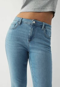 Světlé modré džíny z denimu s úzkým střihem, vysokým pasem, předními kapsami a jemnou vybledlou texturou. Stříbrný knoflík jako akcent.