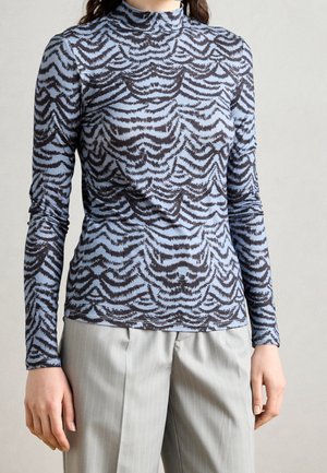 Personne portant un haut moulant à manches longues avec un motif abstrait ondulé bleu et noir et un pantalon gris clair à fines rayures.