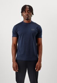 Navy blue fitted t-shirt made of cotton, featuring short sleeves, a round neckline, and a subtle EA7 logo on the chest.