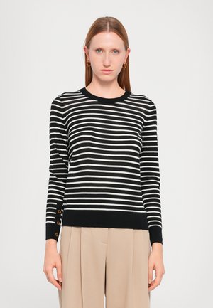 Zwart-wit gestreepte trui met een ronde hals en geribbelde manchetten. Voorzien van knoopaccenten op de manchetten van de mouwen, gecombineerd met beige broek.