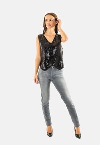 Chaleco negro con brillantes con escote en V y botones, combinado con jeans skinny grises y tacones negros. Textura suave y diseño ajustado.