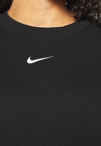 Svart bomullst-shirt med rund halsringning, prydd med en liten vit Nike-logotyp centrerad på bröstet. Slät textur, normal passform.