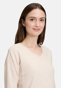 Beiger V-Ausschnitt-Pullover aus weichem Strickstoff, mit einer lockeren Passform und leicht abgesenkten Schultern für zusätzlichen Komfort.