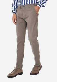 Pantaloni grigi chiari, slim-fit, realizzati in cotone. Presentano tasche laterali, chiusura con bottone e una texture sottile. Indossati con scarpe in suede marroni.