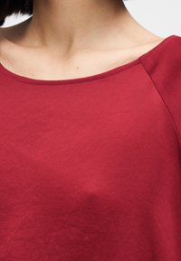 Haut bordeaux à manches courtes avec un large décolleté, fabriqué en tissu lisse, avec une couture nette le long des bords.