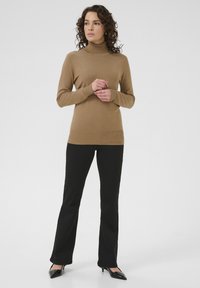 Brązowy sweter z golfem wykonany z miękkiego materiału, o dopasowanej sylwetce, zestawiony z czarnymi spódnicami w stylu dzwonów i czarnymi czółenkami w szpic.