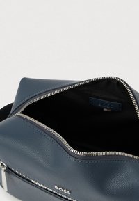 Navyblå lædertaske med tekstureret overflade, lynlåsåbning øverst og sort indvendigt. Har sølvfarvet beslag og mærkelabel indeni.