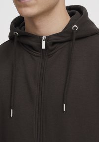 Dark brown zip-up hoodie with a drawstring hood, featuring a smooth texture and silver-colored zipper hardware.