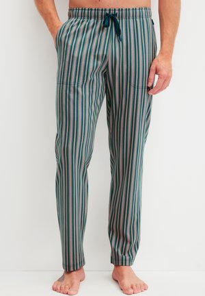 Groen gestreepte pyjamabroek met een elastische tailleband en een marineblauwe trekkoord, gedragen door een persoon zonder schoenen die tegen een witte achtergrond staat.