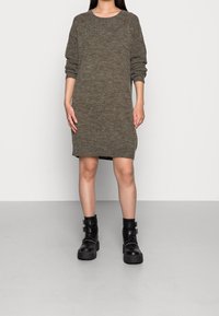 Abito lungo a maniche, lavorato a maglia, in un verde oliva tenue, caratterizzato da una vestibilità comoda, scollatura rotonda e spacchi laterali, abbinato a stivaletti neri con fibbia alla caviglia.