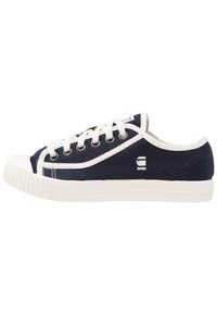 Canvas sneaker in navy blue with white laces, rubber toe cap, and textured white sole. Features a logo on the side and prominent stitching.