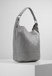 Harmaa nahkainen hobo-laukku, jossa on teksturoitu pinta, kaareva siluetti ja yksi olkahihna. Ominaisuuksiin kuuluu saumaton yläosa ja ommeltu alaosa.