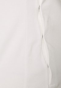 Sweatshirt branco com uma textura lisa, apresentando um fecho lateral com zíper e detalhes de costura visíveis ao longo da costura.