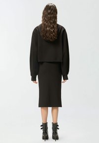 Felpa nera corta con maniche lunghe indossata sopra un abito midi aderente coordinato. Il completo è abbinato a stivaletti neri con dettagli a fiocco.