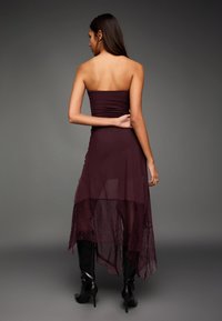 Rochie bordo fără bretele, cu tiv dantelat și din material transparent stratificat, corset mulat și siluetă fluidă. Asortată cu cizme negre până la genunchi.