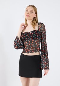 Black floral blouse with long, sheer sleeves and ruched front, featuring red and green patterns. Paired with a form-fitting black mini skirt.