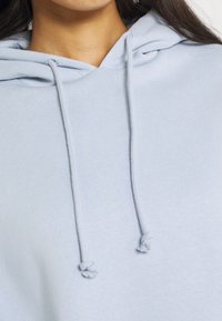 Sweat à capuche bleu clair avec cordons de serrage réglables, texture douce et coupe décontractée. Comprend une capuche et un design minimaliste.