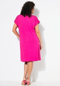 Vestido rosa de largo a la rodilla con mangas cortas, tejido suave y un corte relajado, combinado con sandalias de tacón alto rosas.
