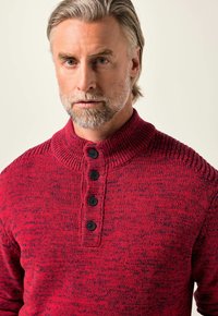 Roter gestrickter Pullover mit hohem Kragen, vier schwarzen Knöpfen und einem strukturierten Muster. Das Material wirkt dick und warm.