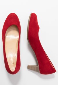 Escarpins en velours rouge à talons hauts avec un bout rond et un talon bloc texturé beige, présentant une semelle intérieure beige lisse avec un logo.