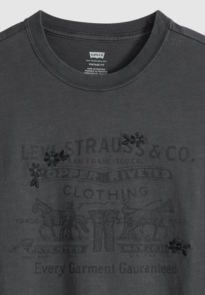 T-shirt Levi's vintage gris foncé avec texte de logo noir délavé et graphique de calèche tirée par des chevaux, agrémenté de fleurs noires brodées.