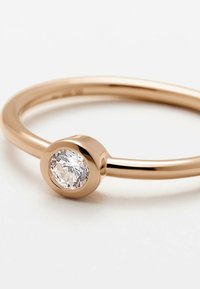 Ring in Roségold mit einem glatten Band und einem runden, in eine Fassung gesetzten klaren Edelstein in der Mitte, der eine polierte, reflektierende Oberfläche zeigt.