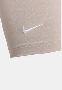 Beige idrottsshorts tillverkade av stretchigt material, med en vit Nike-logotyp. Tätt passande design med en slät yta och rena sömmar.