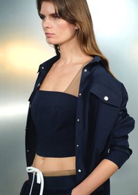 Marineblauw cropped top met een vierkante halslijn, gecombineerd met een bijpassend shirt met zilveren knopen, ontworpen met een beige taillebandaccent.