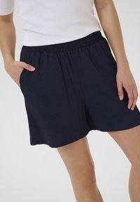 Shorts en bleu marine, texturés, avec une taille élastique et des poches latérales, offrant une coupe décontractée et une finition lisse du tissu.