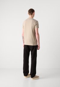 Μπεζ εφαρμοστό μπλουζάκι με κοντά μανίκια, συνδυασμένο με μαύρα παντελόνια, και φορεμένο με μπεζ αθλητικά παπούτσια. Απλός σχεδιασμός, μαλακή υφή, ελάχιστες λεπτομέρειες.