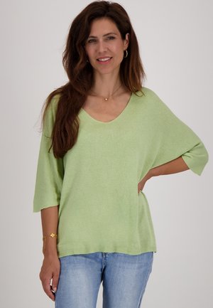 Lichtgroen gebreid sweater met een v-hals, relaxte pasvorm en korte mouwen. Gecombineerd met lichtblauwe jeans. Gladde textuur, minimale details.