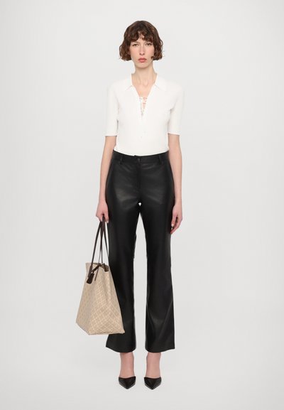 White ribbed top with collar and lace-up detail, paired with black leather trousers. Holding a beige patterned tote bag, wearing black heeled shoes.